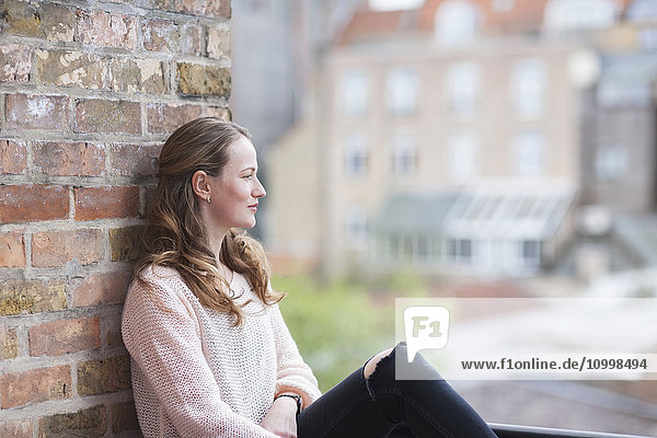 Mid-adult woman sitting and leaning against brick wall