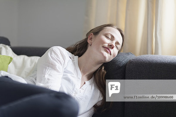 Mittlere erwachsene Frau auf dem Sofa liegend  mit geschlossenen Augen und lächelnd