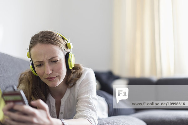 Eine Frau im mittleren Erwachsenenalter liegt auf dem Sofa und hört Musik vom Smartphone