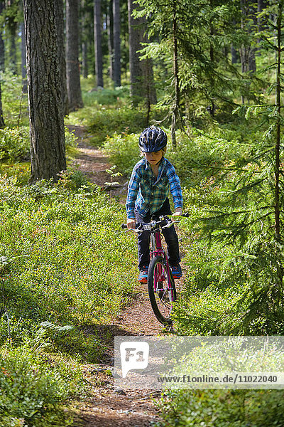 Boy riding bicycle on trail in woods