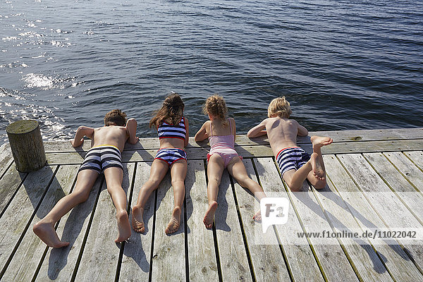 Jungen und Mädchen  die auf dem Dock liegen und auf den See blicken.