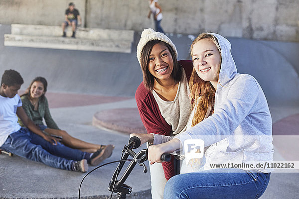 Portrait lächelnde Teenagerinnen mit BMX-Fahrrad im Skatepark