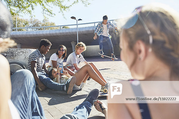 Teenage friends hanging out skateboarding at sunny skate park