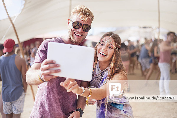 Junges Paar nimmt Selfie mit digitalem Tablett auf dem Musikfestival mit