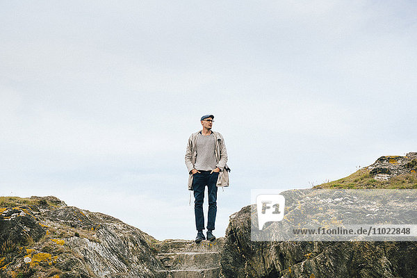 Man looking away while standing on cliff against sky