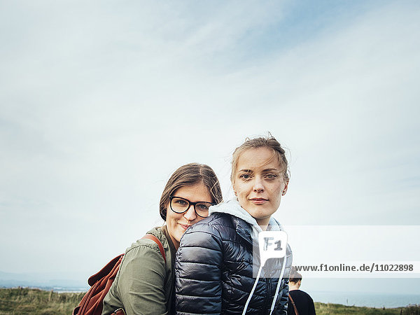 Side view portrait of affectionate female friends against sky