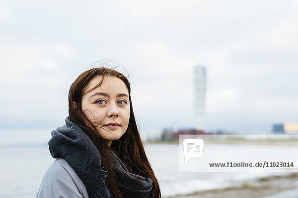 Thoughtful young woman looking away at beach against sky