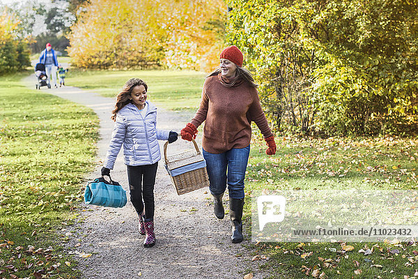 Full length of mother and daughter with picnic basket walking on footpath in forest
