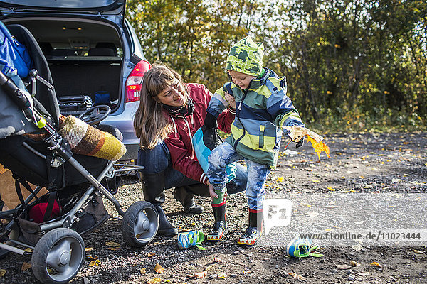 Mature mother assisting boy in wearing rubber boot during picnic