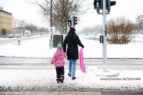 Rear view of woman and daughter with sled walking on snow covered street