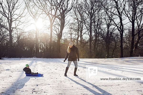 Full length of young woman pulling baby boy on sled