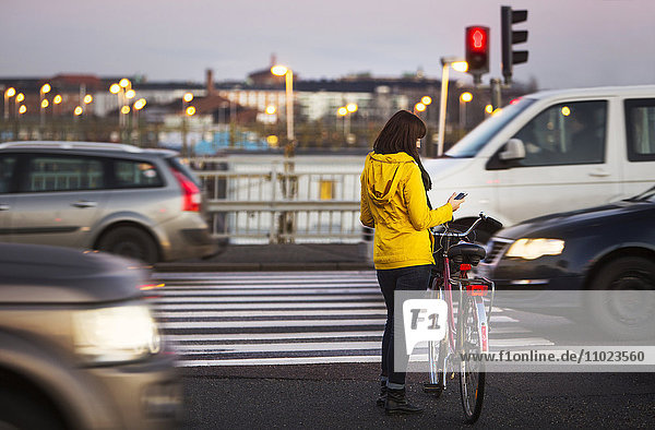 Full length of woman using smart phone while standing with bicycle on city street