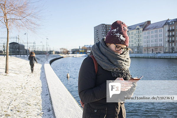Woman using smart phone by canal in city during winter