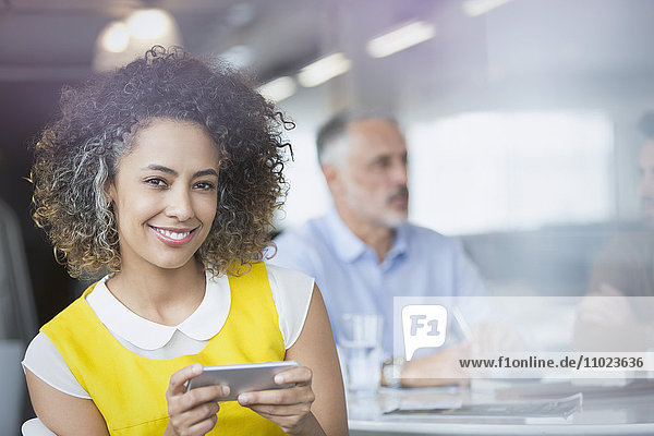 Porträt einer lächelnden Geschäftsfrau  die in einer Besprechung eine SMS mit ihrem Mobiltelefon schreibt