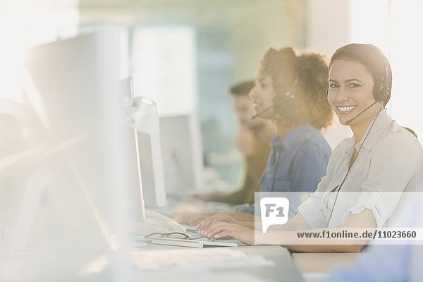 Portrait smiling businesswoman with headset working at computer in office