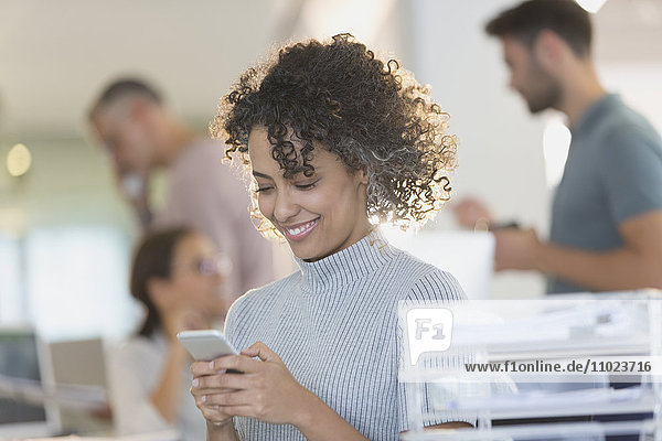 Lächelnde Geschäftsfrau  die mit ihrem Handy im Büro SMS schreibt