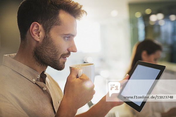 Businessman drinking coffee using digital tablet in office