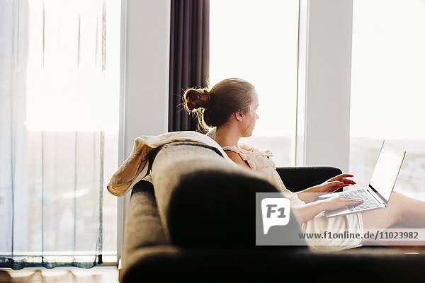 Businesswoman using laptop while relaxing on sofa at hotel room
