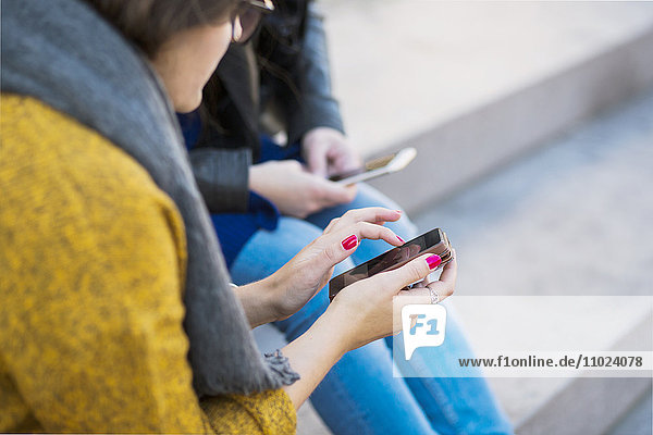 Close-up of women using smart phone while sitting on steps