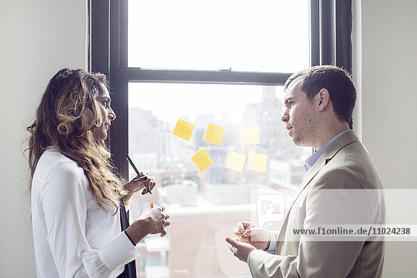 Business people discussing while using sticky notes by window