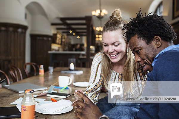 Happy friends looking at smart phone while having coffee