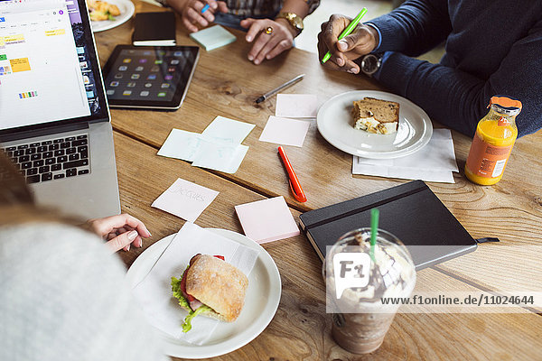 Cropped image of people working while having sandwich at cafe