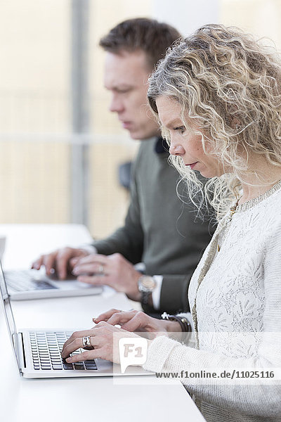 Businesswoman using laptop while sitting with male colleague in office