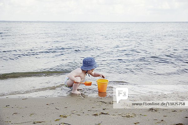 Junge spielt am Strand mit Eimer und Schaufel