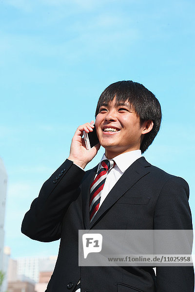 Junger japanischer Geschäftsmann am Telefon
