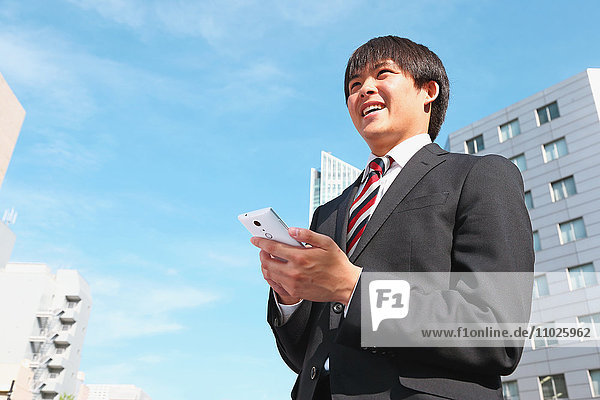 Junger japanischer Geschäftsmann mit Smartphone
