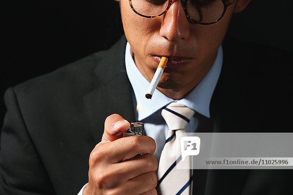 Junger japanischer Geschäftsmann raucht Zigarette