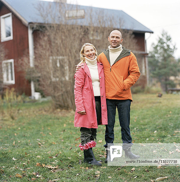 A smiling couple outside their house an autumn day.