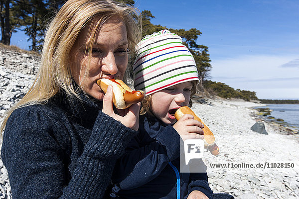 Mutter und Sohn essen Hot Dogs am Strand