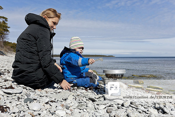 Mother with son cooking on rocky beach