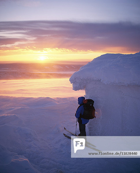 A skier watching a sunset in a winter landscape.