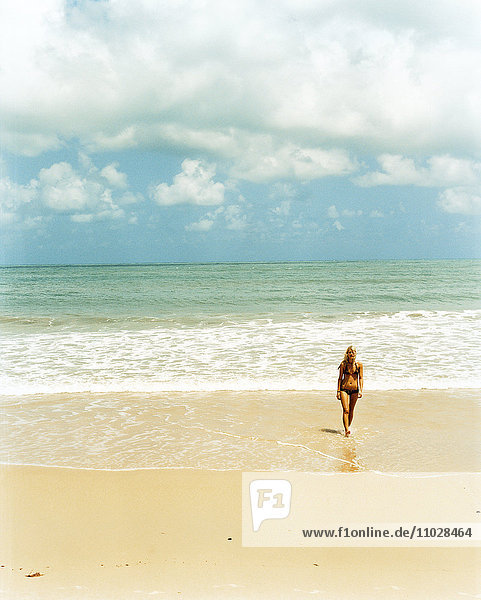 A woman walking on a sandy beach.