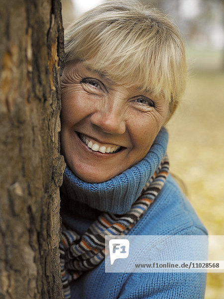 Eine lächelnde Frau hinter einem Baumstamm  Porträt.