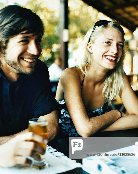 Ein lächelnder junger Mann und eine lächelnde Frau in einem Café unter freiem Himmel.