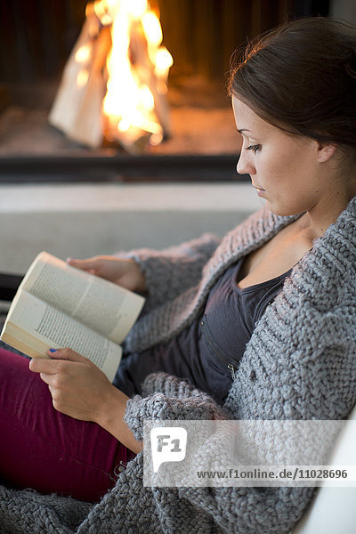 Young woman sitting in front of fireplace and reading