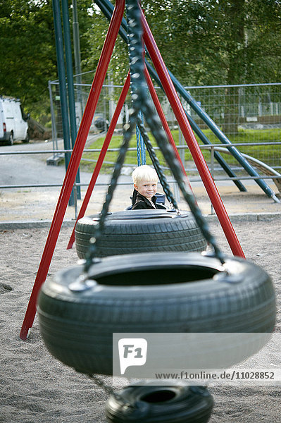 Junge auf Spielplatz  Reifenschaukel im Vordergrund