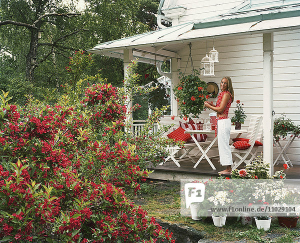 Frau steht auf Veranda  umgeben von Rosen