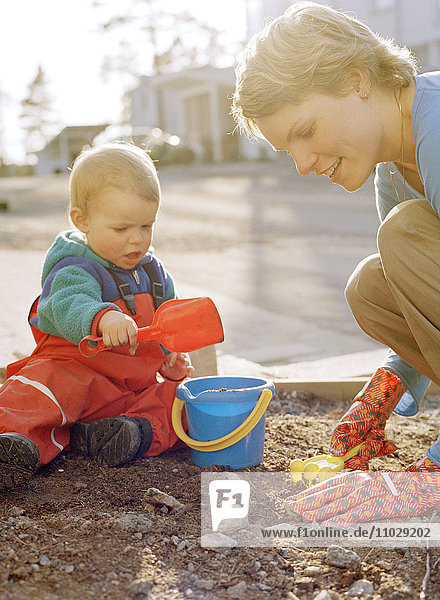 Eine Frau und ein Kind spielen in einem Sandkasten.