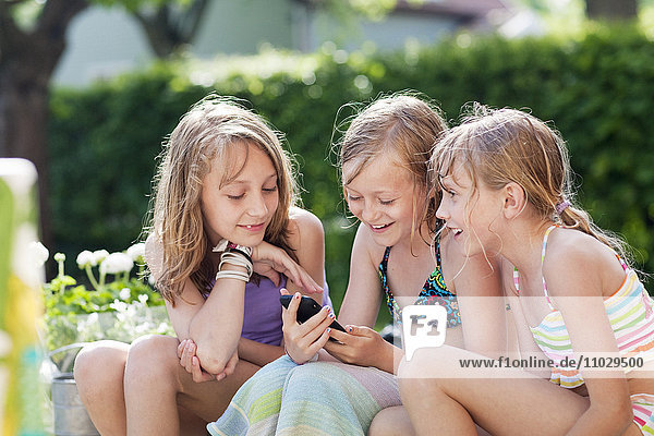 Drei Mädchen sitzen im Garten und schreiben eine SMS mit ihrem Handy
