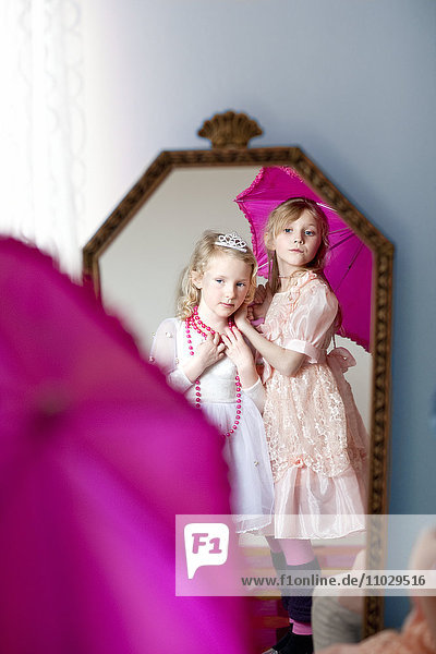 Zwei Mädchen in eleganten Kleidern und Halsketten schauen in den Spiegel