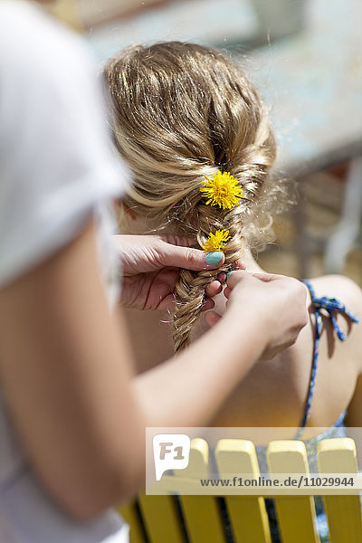 Mädchen flechtet Löwenzahnblüten in das Haar ihrer Freundin
