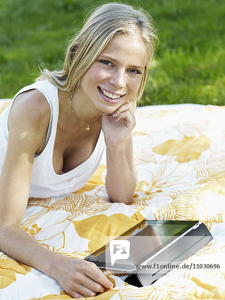 Junge Frau auf Decke liegend mit digitalem Tablet  lächelnd  Porträt