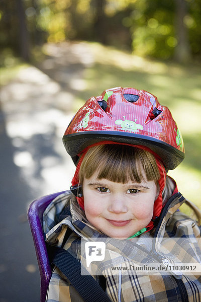 Porträt eines Mädchens mit Helm auf einem Kindersitz auf einem Fahrrad