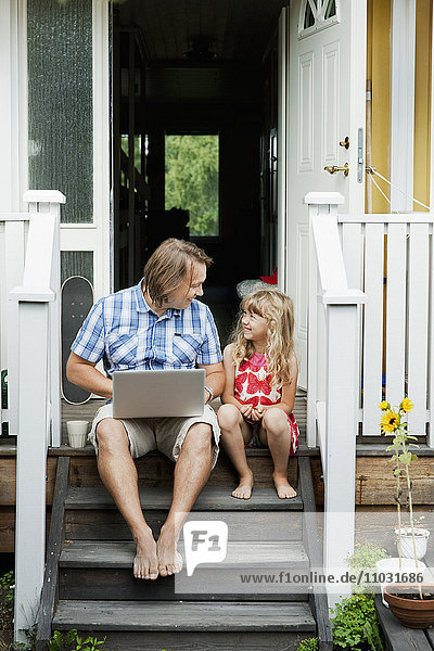 Vater mit Tochter sitzt auf den Stufen vor dem Haus mit Laptop  Sollentuna  Stockholm  Schweden