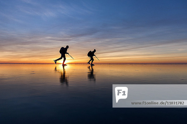 Menschen beim Schlittschuhlaufen bei Sonnenuntergang  Vanern  Schweden