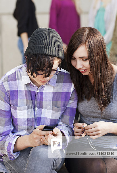 Zwei Jugendliche sitzen auf einer Bank mit einem Mobiltelefon